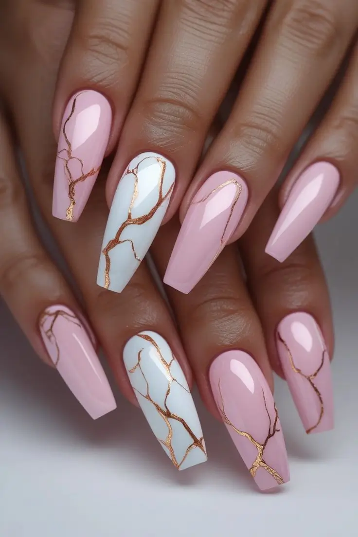 Close-up of a hand with long coffin nails featuring rose quartz marble nail art, combining solid blush pink with white marble and delicate gold vein accents, showcasing an elegant and trending design for US manicures.