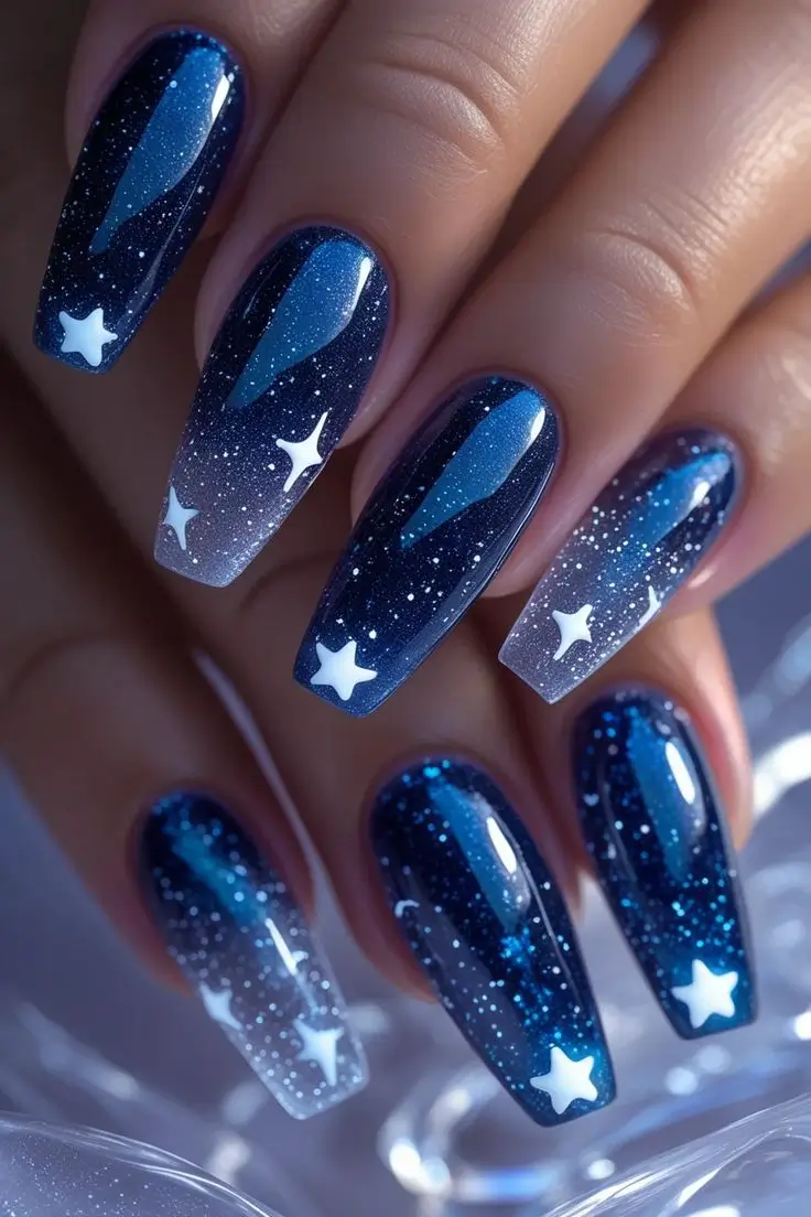 Close-up of a hand with long coffin nails featuring a starlight cosmic veil nail art design with deep blue galaxy ombre, white stars, and subtle glitter for a mystical and trending USA manicure.