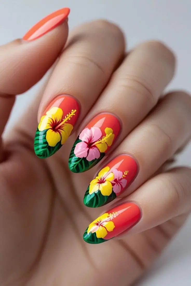 Close-up of a hand with vibrant coral red almond nails featuring hand-painted tropical hibiscus flowers in yellow and pink with green leaves, showcasing a beautiful summer floral nail art trend popular in the USA.