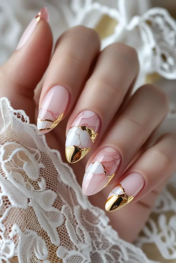 Close-up of a hand with almond nails featuring elegant rose quartz and white marble nail art with gold foil accents and a gold chrome tip, showcasing a luxurious natural stone-inspired design trending in US manicures.