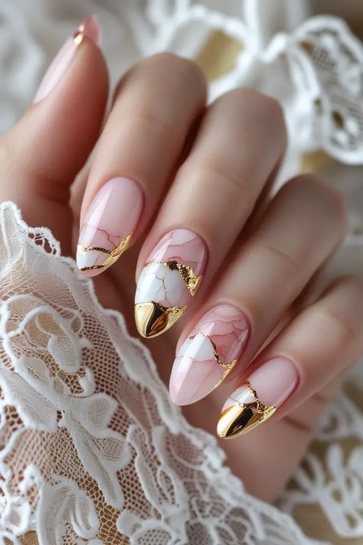 Close-up of a hand with almond nails featuring elegant rose quartz and white marble nail art with gold foil accents and a gold chrome tip, showcasing a luxurious natural stone-inspired design trending in US manicures.