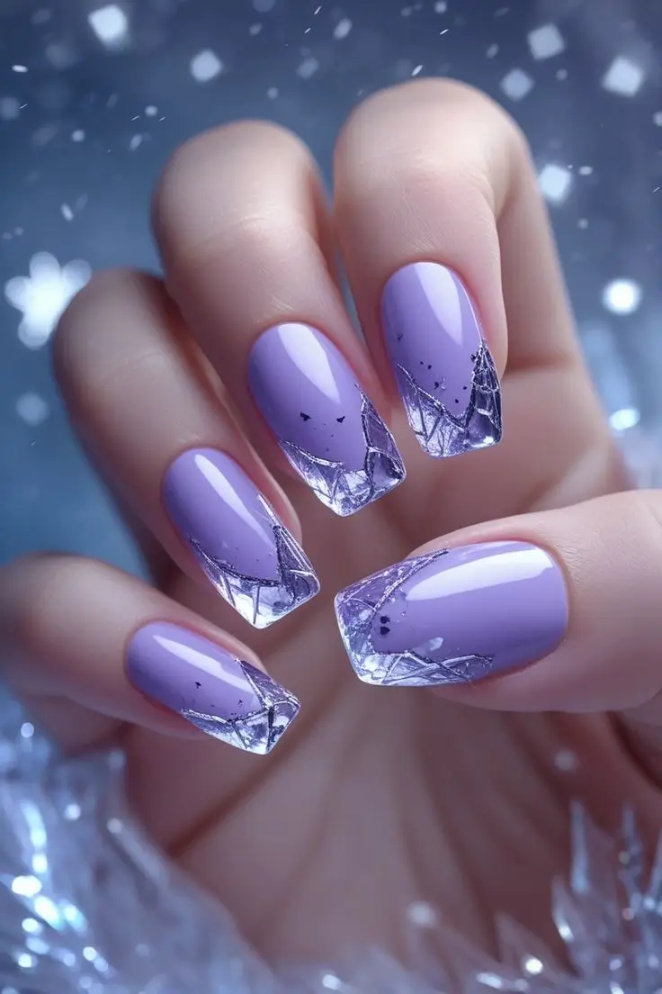 Close-up of a hand with square-shaped nails featuring frozen lavender crystal nail art with a lavender ombre fade to clear tips with silver geometric ice patterns, showcasing a chic and trending winter design for US manicures.