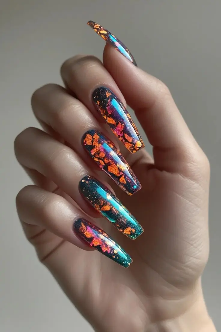 Close-up of a hand with long coffin nails featuring mesmerizing iridescent fire opal crystal nail art with multi-color shifting flakes in orange, red, purple, and blue on a dark base, showcasing a luxurious and trending design for US manicures.