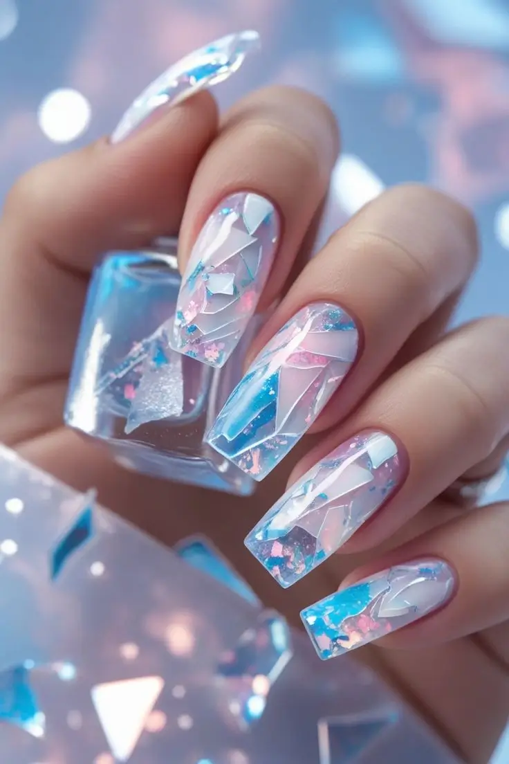 Close-up of a hand with long coffin nails featuring opal ice shard nail art design with clear, frosted elements and iridescent flakes reflecting pink, blue, and white, showcasing a chic and trending winter manicure in the USA.