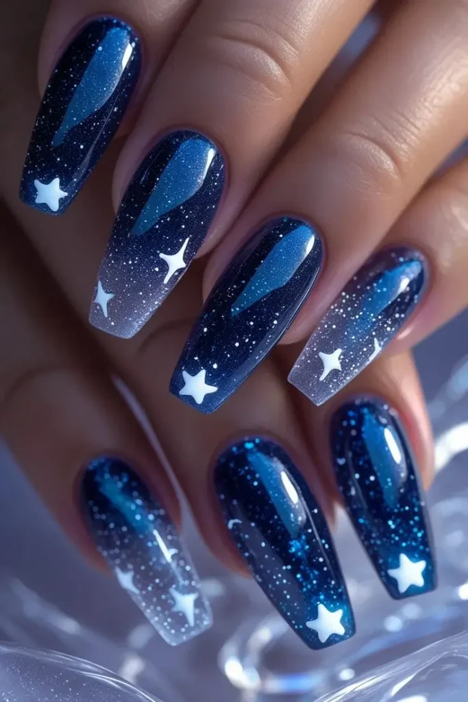 Close-up of a hand with long coffin nails featuring a starlight cosmic veil nail art design with deep blue galaxy ombre, white stars, and subtle glitter for a mystical and trending USA manicure.
