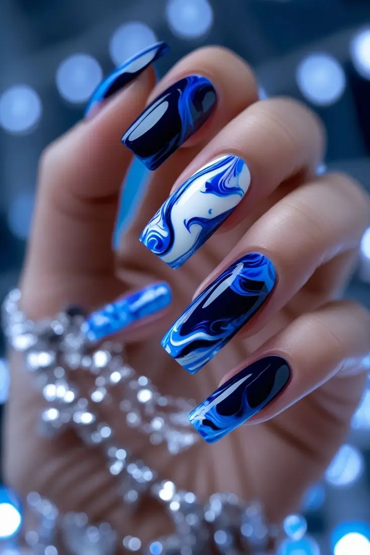 Close-up of a hand with long coffin nails featuring blue fire marble nail art with swirling patterns of navy blue, vibrant blue, and white, showcasing an electric and trending design for US manicures.