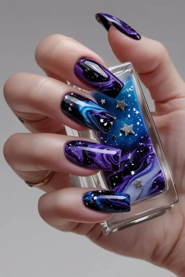 Close-up of a hand with long square nails featuring galactic marble glitter nail art with swirling purple, blue, and black cosmic patterns, silver glitter, and star foils, showcasing a mystical and trending design for US manicures.
