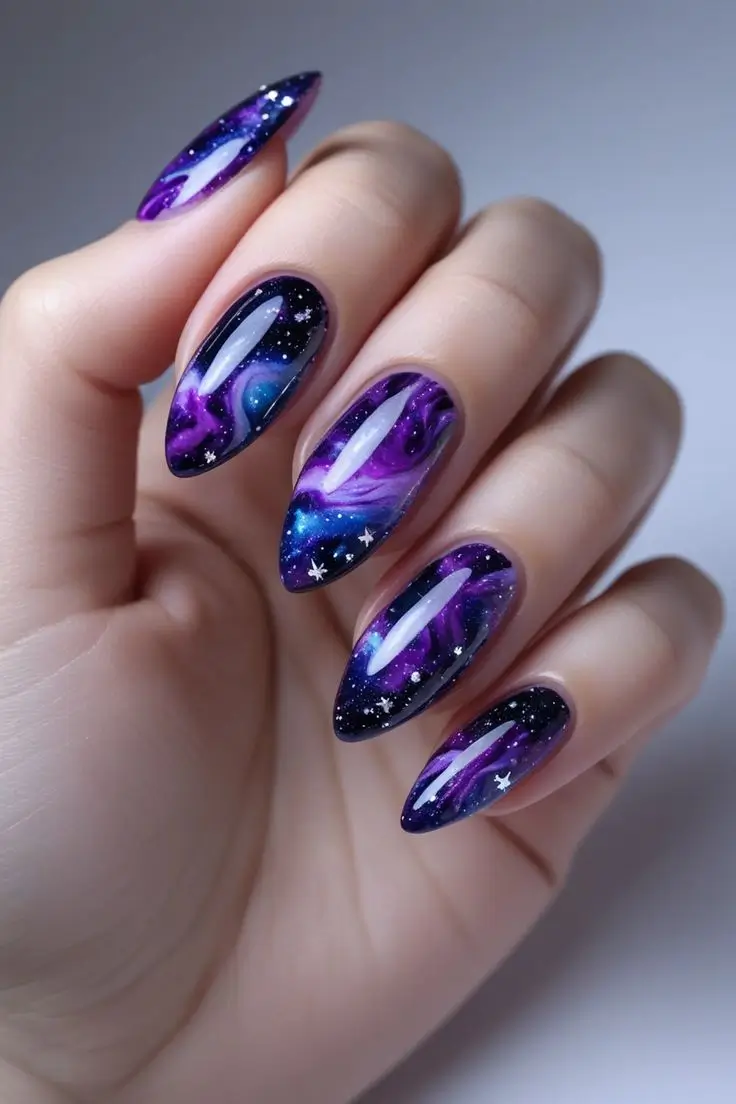 Close-up of a hand with long almond nails featuring galactic smoke marble nail art with swirling purple, blue, and black cosmic patterns, silver accents, and white stars, showcasing a mystical and trending design for US manicures.