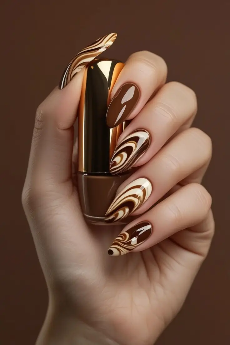 Close-up of a hand with long almond nails featuring glossy mocha swirl nail art with caramel, espresso, and cream marble patterns, showcasing a sophisticated and trending design for US manicures.