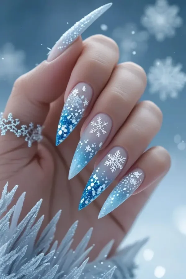Close-up of a hand with long stiletto nails featuring ice queen frosted French tips with a blue and white glitter gradient and white snowflakes, showcasing a winter-inspired and trending design for US manicures.
