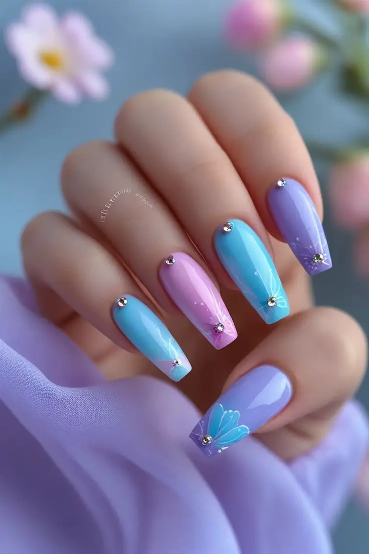 Close-up of a hand with long coffin nails featuring pastel butterfly dream nail art with pink, blue, and lavender colors, hand-painted wing details, and clear rhinestones, showcasing a whimsical and trending design for US manicures.