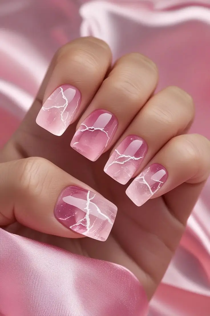 Close-up of a hand with square nails featuring rose quartz crystal nail art with a translucent pink base and white crackle patterns, showcasing a gem-inspired and trending design for US manicures.