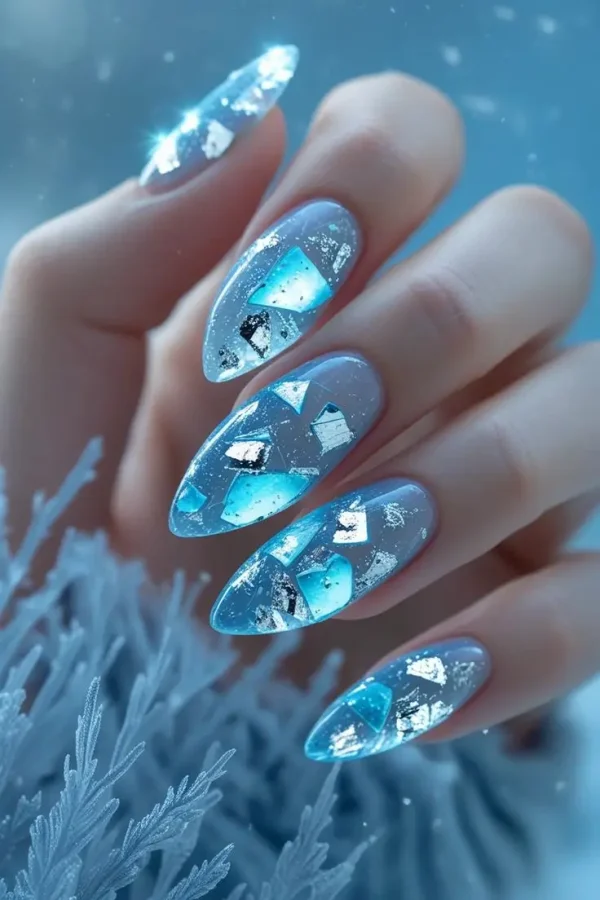 Close-up of a hand with long stiletto nails featuring icy blue crystal shatter nail art with iridescent holographic foil embedded in a translucent, glossy finish, showcasing a frozen-inspired and trending design for US manicures.