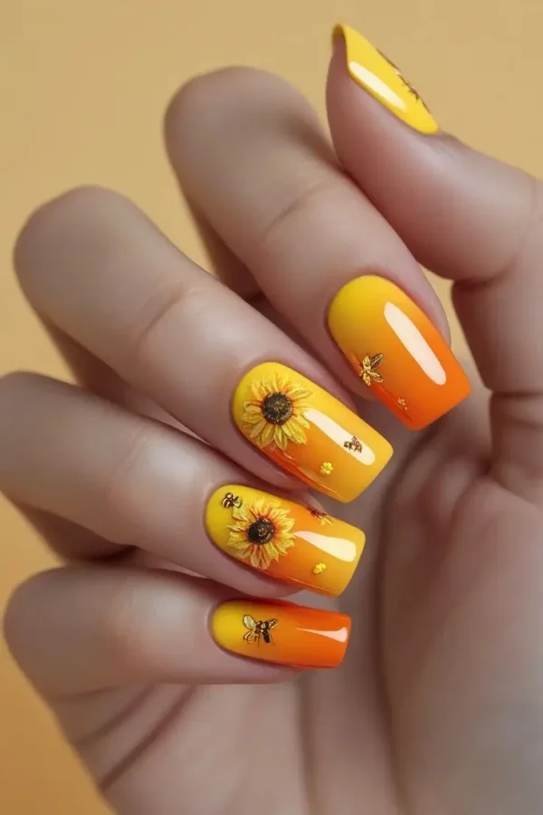 Close-up of a hand with coffin nails featuring a sunflower honey ombre nail design with a yellow to orange gradient, hand-painted sunflowers, and bee decals, showcasing a summer-inspired and trending design for US manicures.